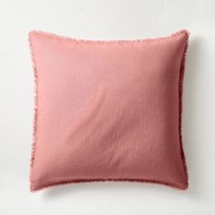 a pink pillow on a white surface with a light colored linen backing and frayed edges