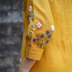 a person wearing a yellow shirt with blue and white flowers embroidered on it's sleeves