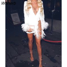 a woman in a white dress with feathers on her body and heels, posing for the camera