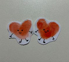 two heart shaped stickers with faces drawn on them, one is orange and the other is white