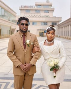 a man and woman standing next to each other in front of a building with white flowers