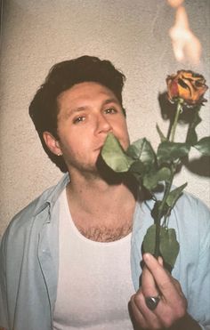 a man holding a rose in front of his face and blowing it out to the side