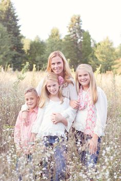 three girls are standing in the middle of a field with tall grass and trees behind them