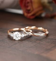 two wedding rings on a wooden table with flowers in the backgroung and one diamond ring