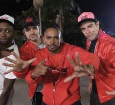 four men in red jackets and hats posing for the camera with their hands up while one man holds out his hand