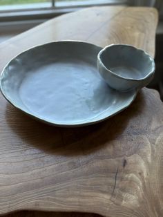 two white bowls sitting on top of a wooden table next to a window sill