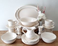 a table topped with lots of white dishes and cups on top of a wooden table