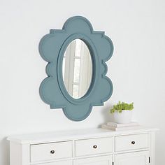 a white dresser with a blue mirror on the wall above it and a potted plant