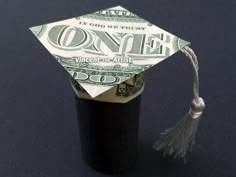 an origami graduation cap on top of one hundred dollar bills with a tassel