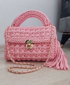 a pink crocheted purse with a tasselled handle and gold hardware, sitting on a wooden surface