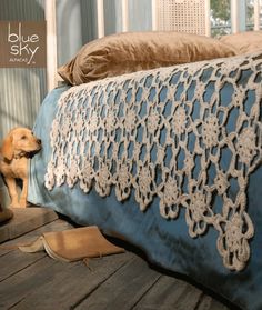 a dog sitting on the floor next to a crocheted bedspread and pillow