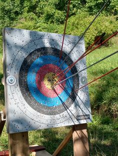 an archery target with arrows in the center on a wooden stand near grass and trees