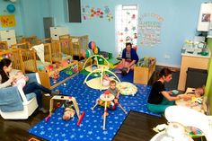 a group of people sitting around in a room with blue walls and wooden floors, while one woman holds a baby