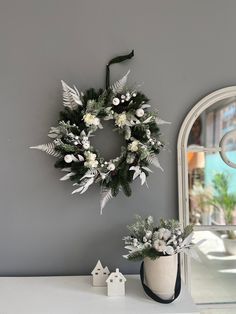 a wreath on the wall next to a vase with flowers and greenery in it