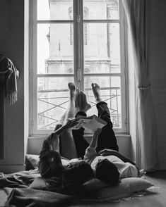 two people laying on the floor in front of a window with their feet propped up