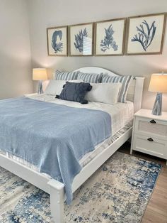 a bed with blue and white pillows in a bedroom next to two framed pictures on the wall