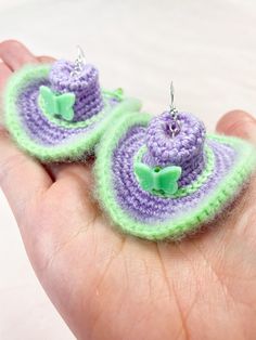 two small crocheted items in the palm of someone's hand, one is purple and green