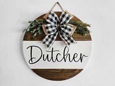 a wooden sign that says dutcher hanging on a white wall with a black and white bow