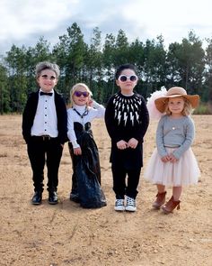 three children dressed up in costumes standing on dirt ground with trees in the backgroud