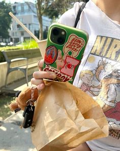 a person holding a cell phone in their right hand and a bag with a teddy bear on it