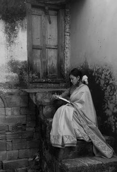 an old photo of a woman sitting on some steps reading a book while holding a flower in her hair