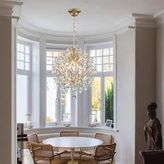 a dining room table with chairs and a chandelier hanging from the ceiling in front of two windows