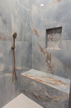 a shower with marbled walls and flooring next to a tiled wall in a bathroom