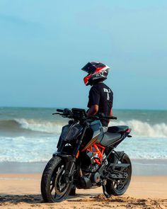 a man standing on top of a motorcycle next to the ocean in front of waves