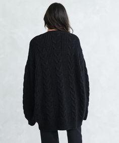 the back view of a woman wearing a black cable knit cardigan sweater with long sleeves