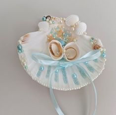 a white shell with pearls and baby shoes on it's head is adorned with blue ribbon