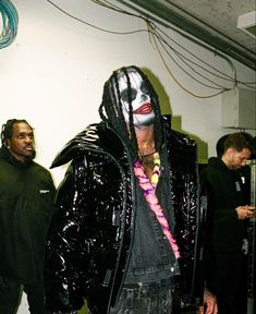 a man dressed in black and wearing a mask with his hair pulled back, standing next to other men