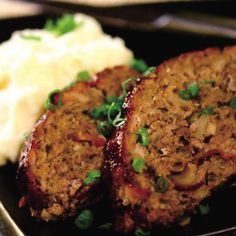 meatloaf with mashed potatoes and green onions on a black plate, ready to be eaten