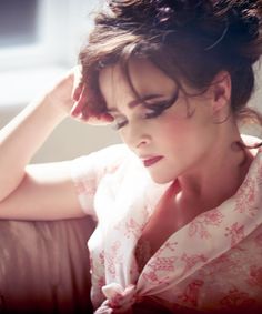 a woman sitting down with her hand on her head and looking at the camera while wearing a blouse