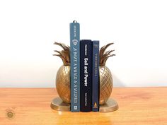 two books sit on top of each other in front of a gold pineapple shaped bookend