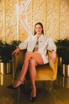 a woman is sitting on a chair in front of a wall with a neon sign