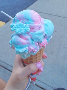 a hand holding an ice cream cone with blue, pink and green toppings