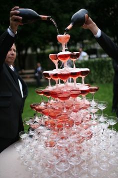 two people pouring wine into glasses on top of a table covered in champagne flutes and plates