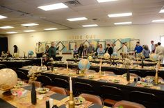 a group of people standing around tables with place settings on them and balloons hanging from the ceiling