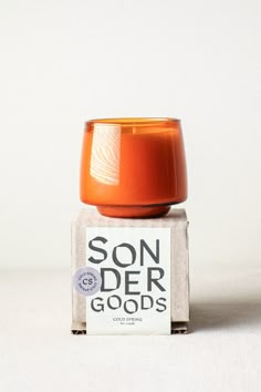 an orange candle sitting on top of a carton that says son der goods in white lettering