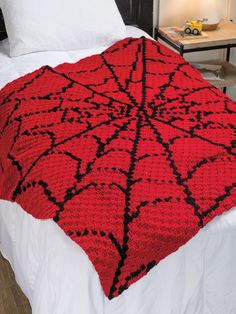 a red and black crocheted blanket sitting on top of a bed next to a night stand