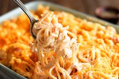 a spoon full of macaroni and cheese being lifted from a casserole dish