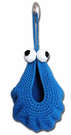 a crocheted blue bag with eyes hanging from it's side, on a hook