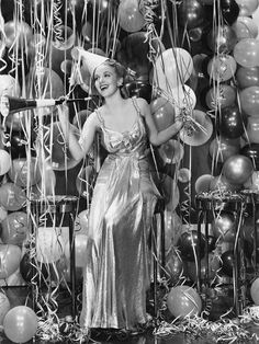 an old photo of a woman standing in front of balloons and confetti sticks