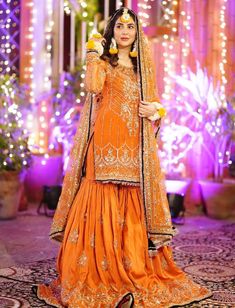 a woman in an orange dress standing on a stage with lights behind her and flowers in her hair