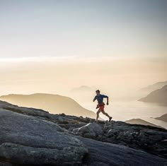 a man running on top of a rocky hill next to the ocean in the distance