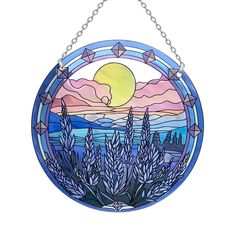 a stained glass window hanging on a chain with the sun setting in the distance behind it