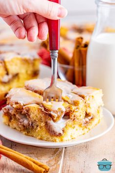 a person is holding a fork over a piece of cinnamon roll on a white plate