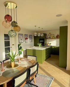 a dining room table and chairs in front of an open kitchen with green cabinetry