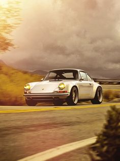 a white porsche parked on the side of a road near trees and hills with clouds in the background