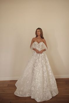 a woman in a white wedding dress standing against a wall with her hands on her hips